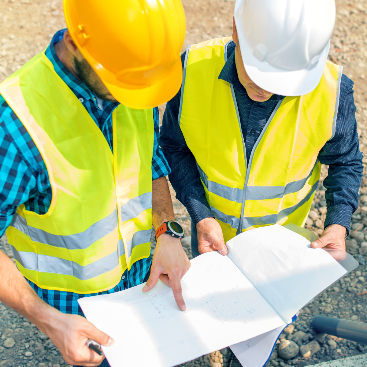 Two construction workers in high-visibility vests and hard hats reviewing building plans on-site.