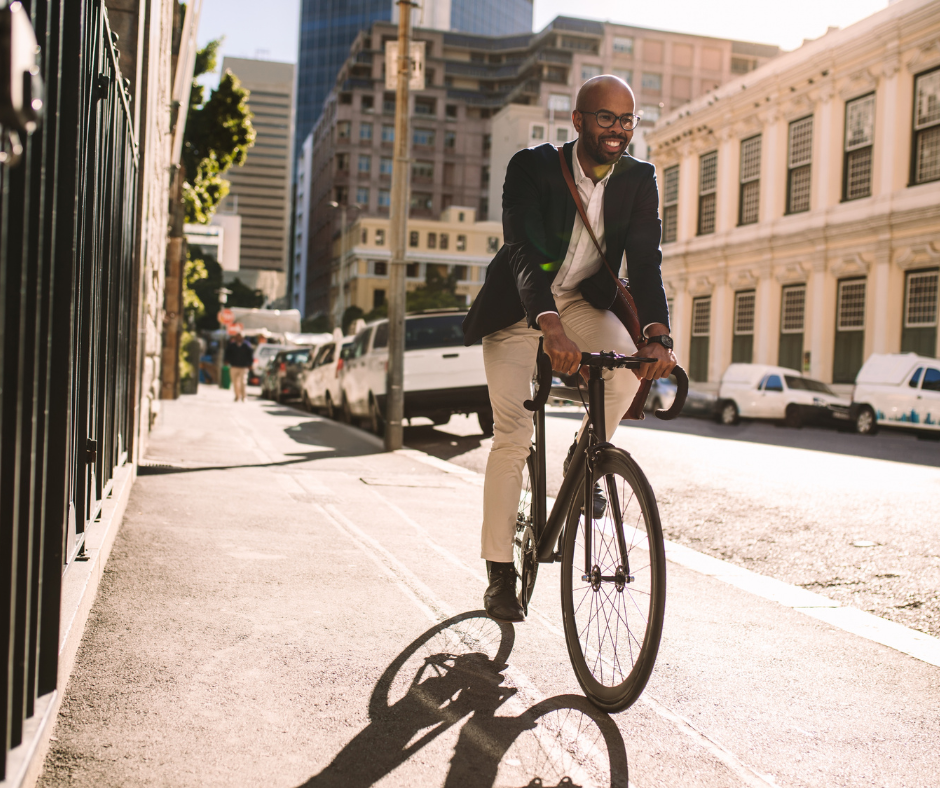 Business professional cycling to work through a city street in sunlight, wearing a blazer and carrying a shoulder bag